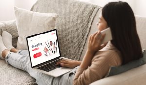Female Shopping Concept. Back view of woman browsing online make up store, talking on phone, sitting at home. Online Beauty Stores in Canada. Nail supplies. nail stores. Best nail stores.