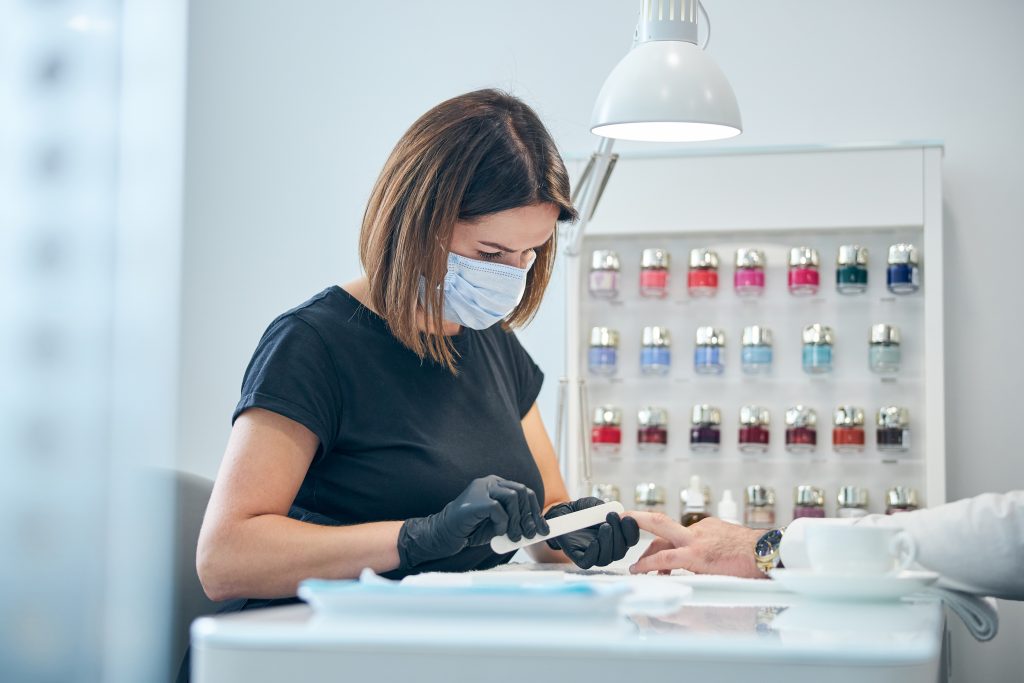Attentive young beauty master sitting at her workplace while doing manicure for her client