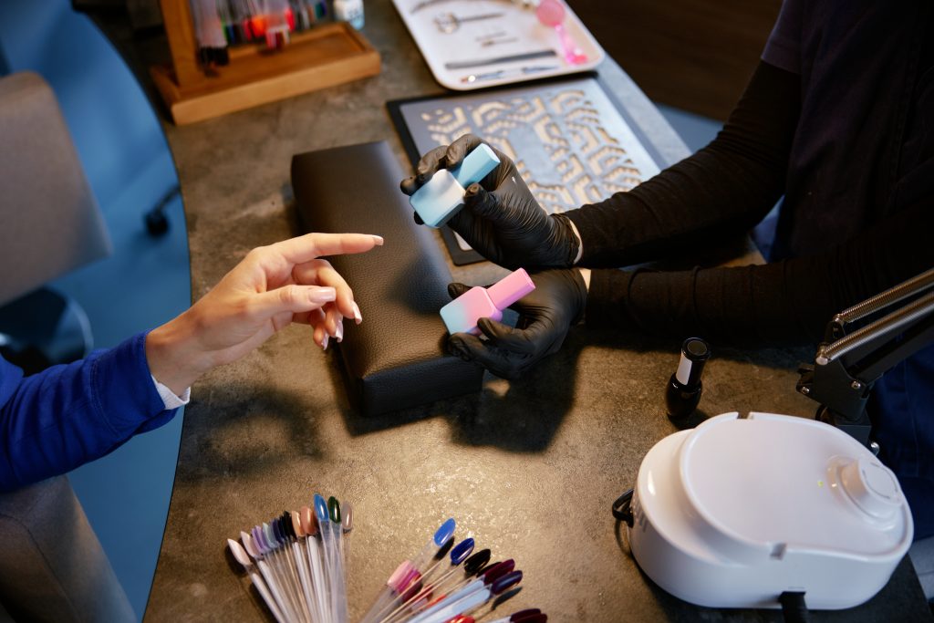 Professional manicurist offering colorful nail polish flask to client closeup view from above. Manicure studio concept