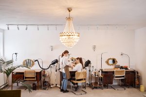 Hair Salons in Canada. Wide angle view of luxury grooming salon with crystal chandelier and two women caring for cute dog copy space