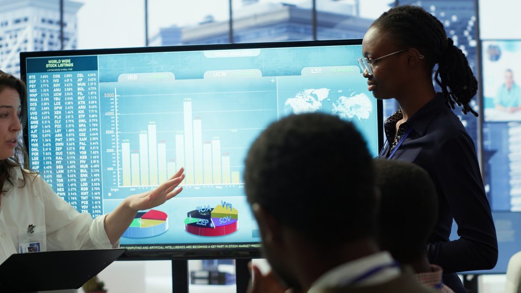 Coworkers engaging in a problem solving meeting at a corporation, using an interactive board to visualize data and develop solutions for complex business challenges. Analysis presentation. Camera A.