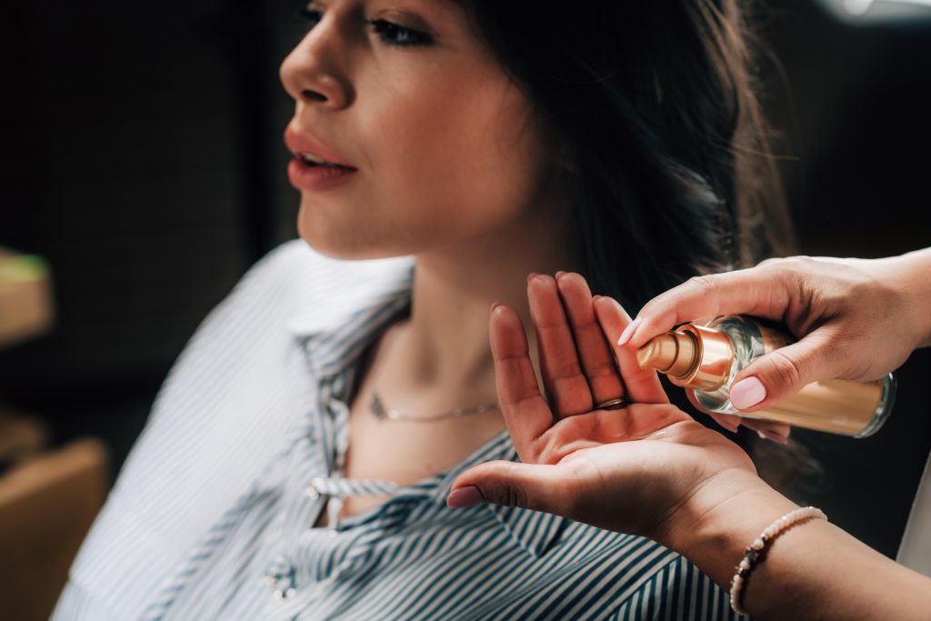 Hairdresser applying revitalizing serum drops on woman’s long black hair