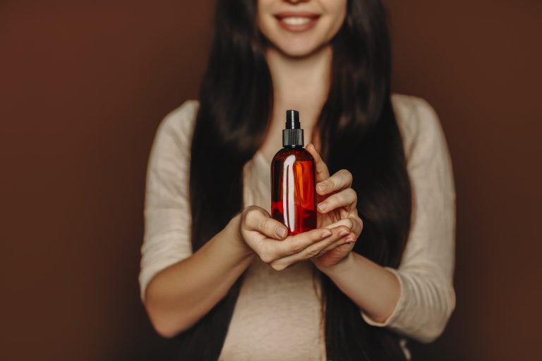 Studio portrait of happy satisfied woman holding her long healthy brown hair and showing at camera shampoo or conditioner, female using natural paraben free hair-care beauty products, selective focus