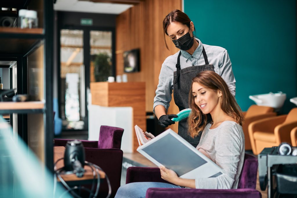 Young happy woman choosing hair color from catalog while being at hairdresser's during coronavirus pandemic in a hair salon in Ottawa