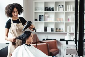 Hair Salon in Ottawa. African american hairdresser drying hair of young customer, empty space