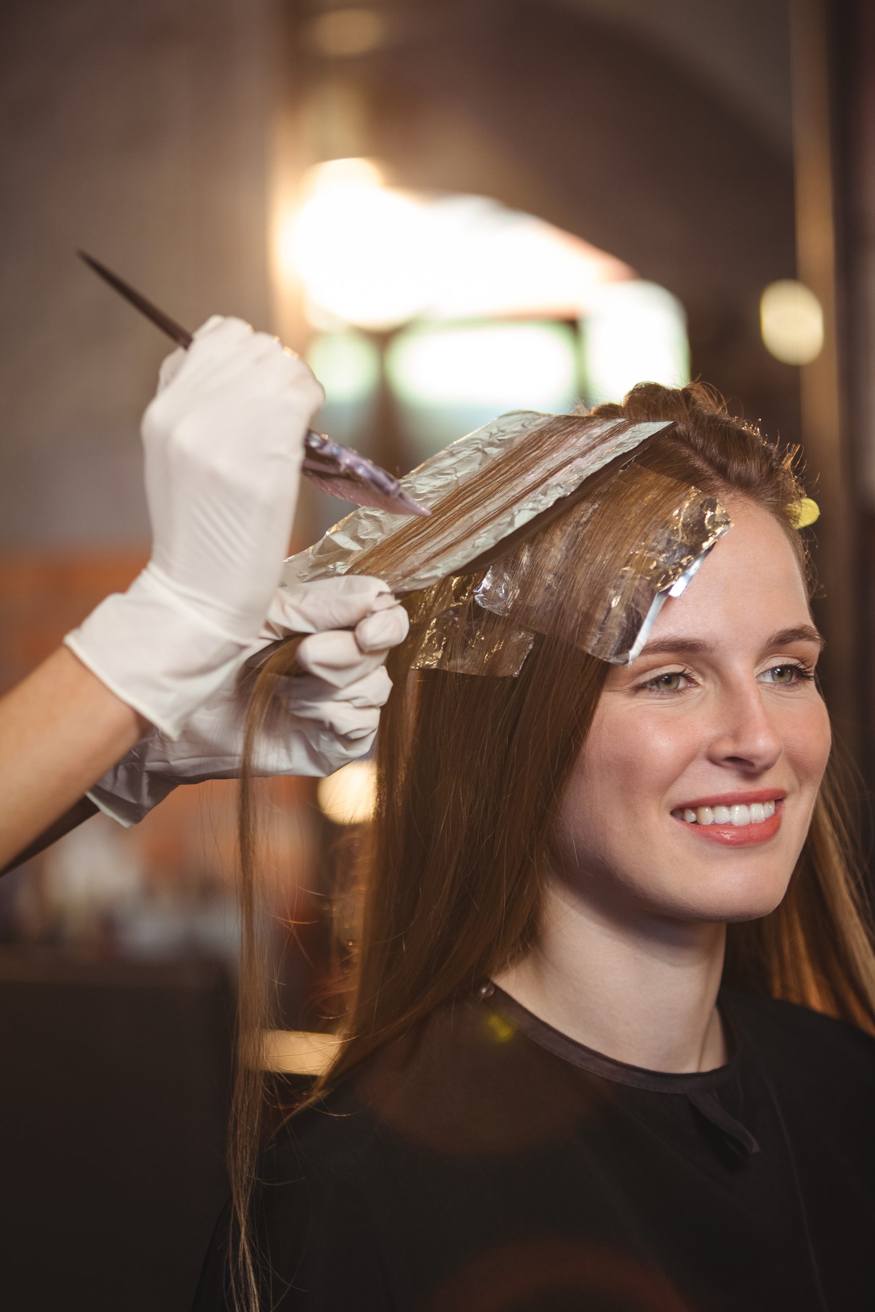 Hair Color Prices. How Much Does Hair Color Cost in hair salon, woman getting her hair dyeing at a hair salon.