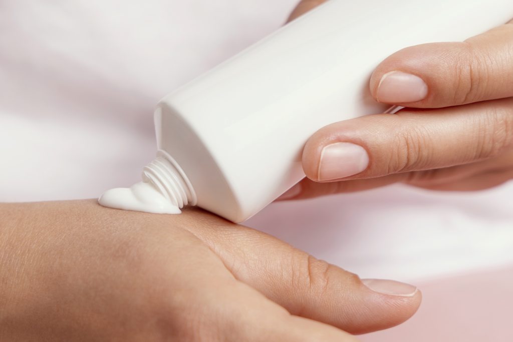 Close up of woman in white t-shirt squeezing hand cream on a hand and holding a tube in other hand. Beauty treatment or handcare procedure in a spa salon, natural cosmetics mockup
