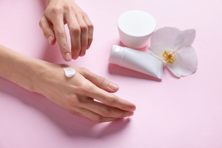 Woman with hand creams and orchid on pink background, closeup