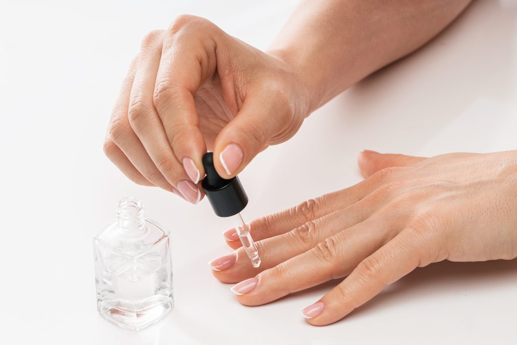 Female hands and bottle of nourishing cuticle oil with a dropper on white background. Strengthen Natural Nails.