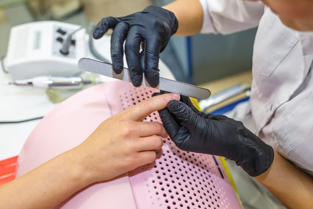 the master in black gloves in the salon makes manicure pedicure to the client