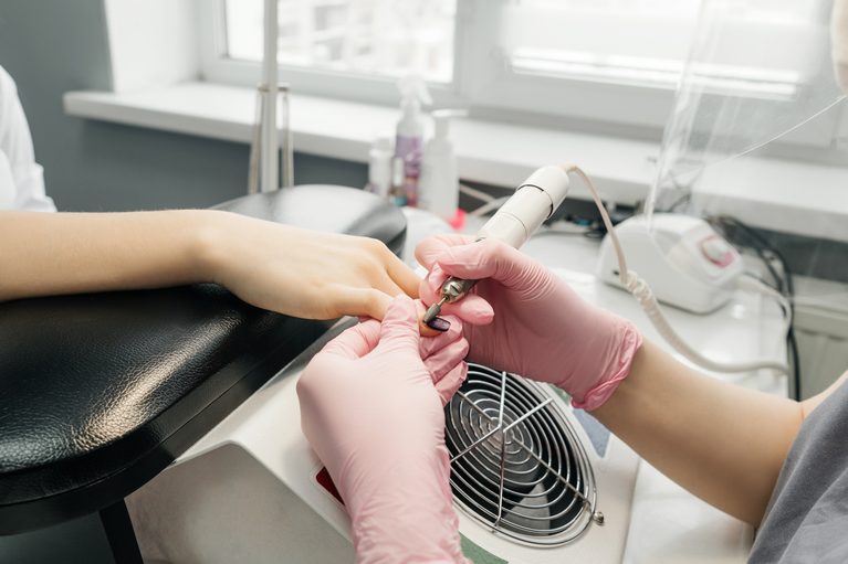 Young woman getting manicure in beauty salon. Manicurist remove old manicure. Women in protective masks, pandemic.